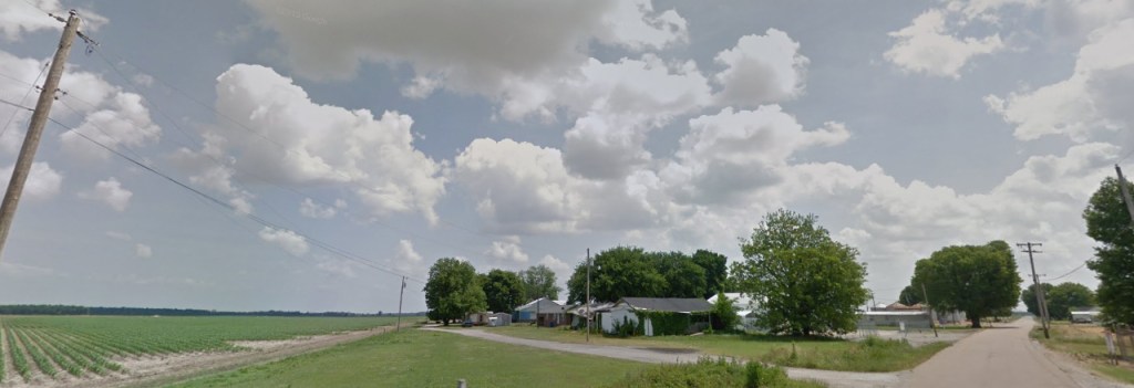 Paved and gravel roads. Farm fields and small houses. Blue sky with clouds on a sunny day.
