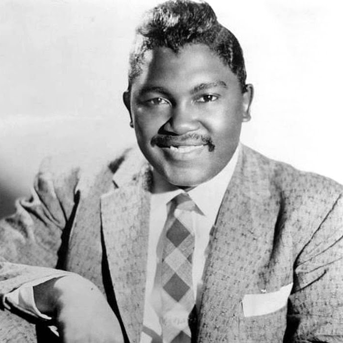 Photo of an African American man from the 1950s. Suit and tie. Pomaded hair, a pocket square, and a smile.