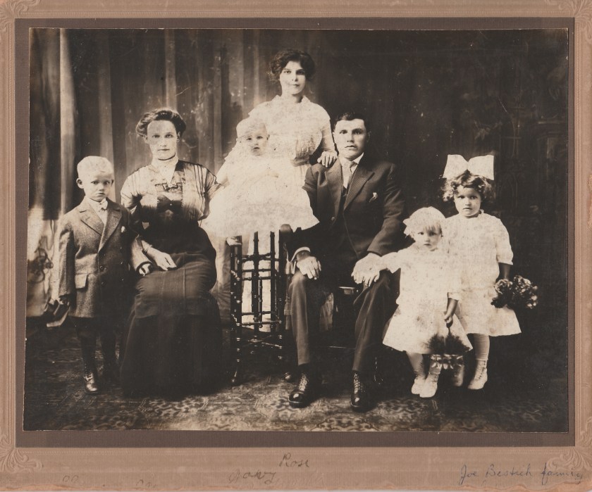 A historic family portrait featuring several adults and children, posed in a studio setting with elegant clothing and accessories.
